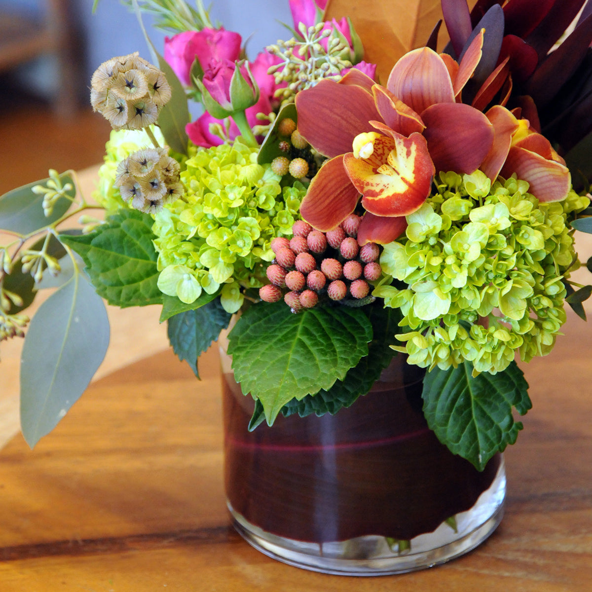 Colorful fall inspired Spruce  flower arrangement in a glass vase on a wooden surface