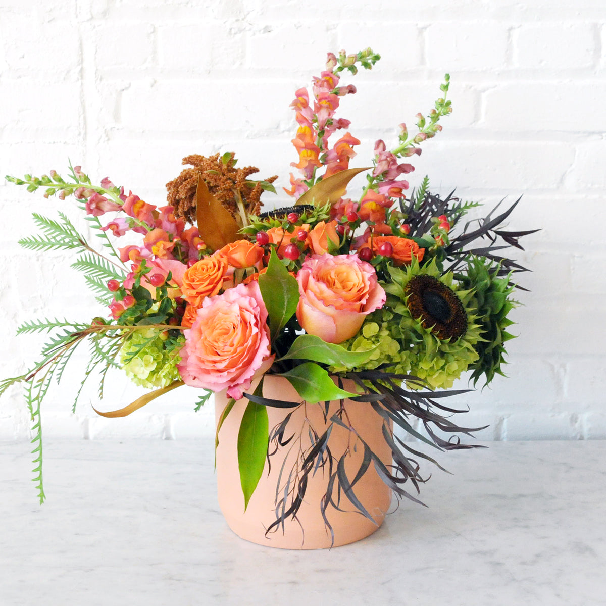 A Fall inspired floral arrangement arranged in a  modern whimsical style. 
Warm oranges reflect the season with textural accents in matt terracotta pot. 