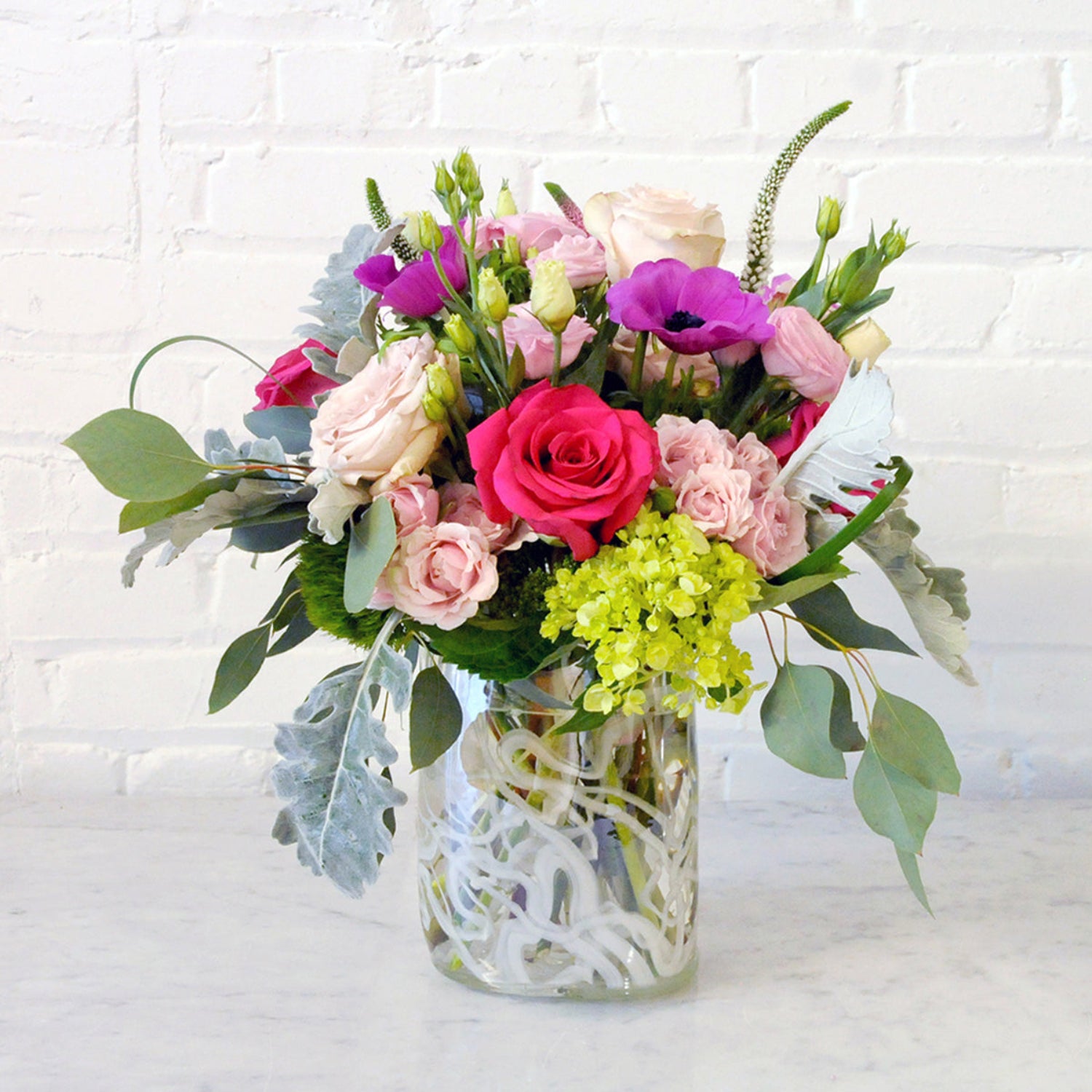 Front View of Edgerton Floral Arrangement showcasing roses, anemone, and lisianthus in a tall clear glass vase with a white swirl pattern 