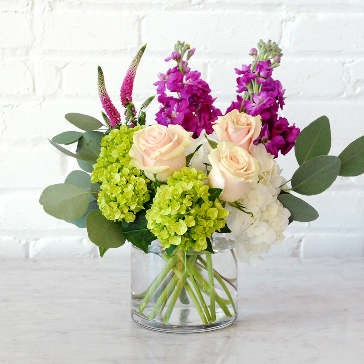 Spruce Flowers Queen Floral arrangement, White and Green Hydrangea with Pink Mondial roses and Hot Pink scented Stock set in a glass vase 