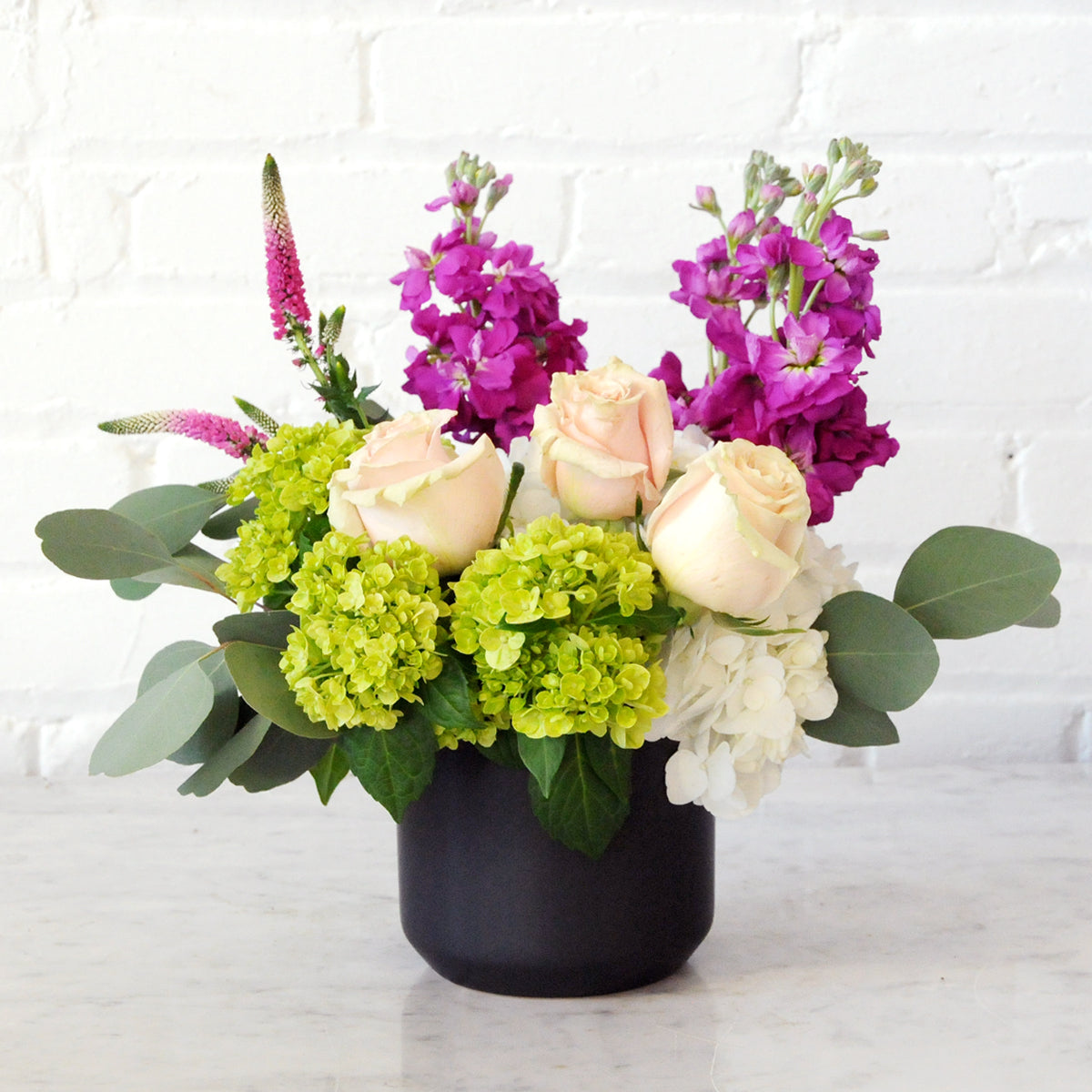 Spruce Flowers Queen arrangement with White and Green Hydrangea, Pastel Pink roses and hot pink stock accents set in a black ceramic vase 