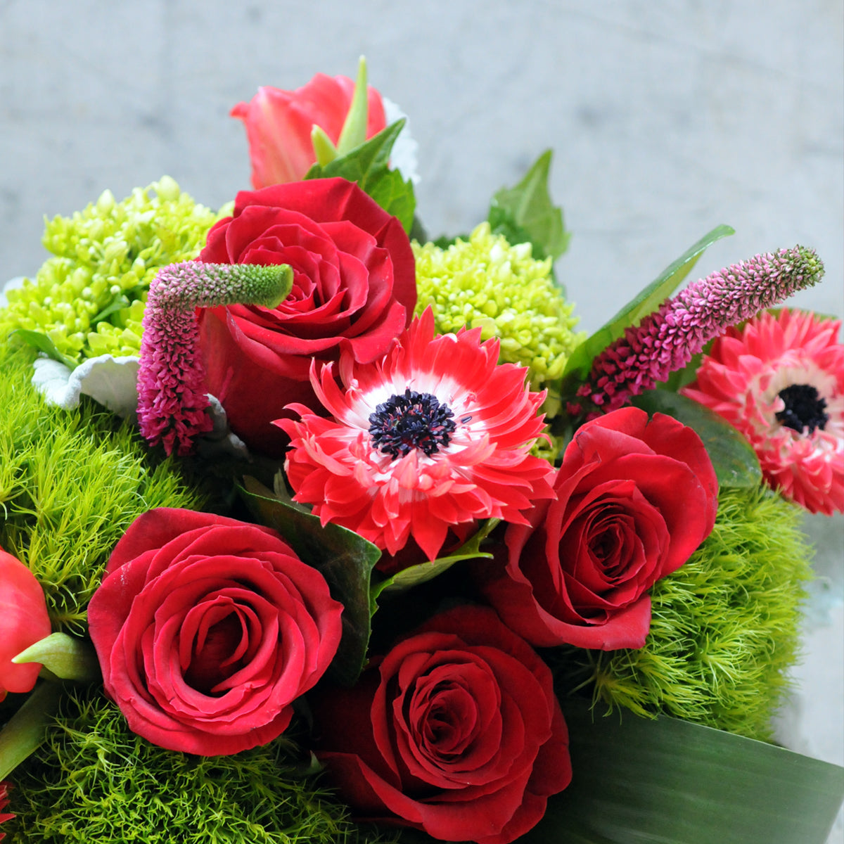 Bouquet of red roses and anemone  with greenery on a light background