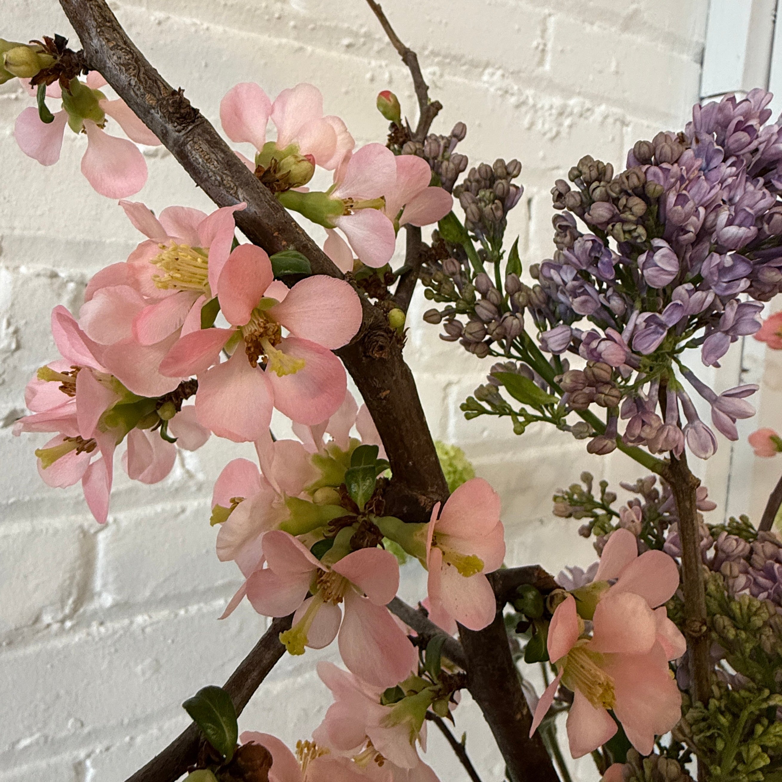 Floral arrangement with pink and purple flowers against a white brick wall.