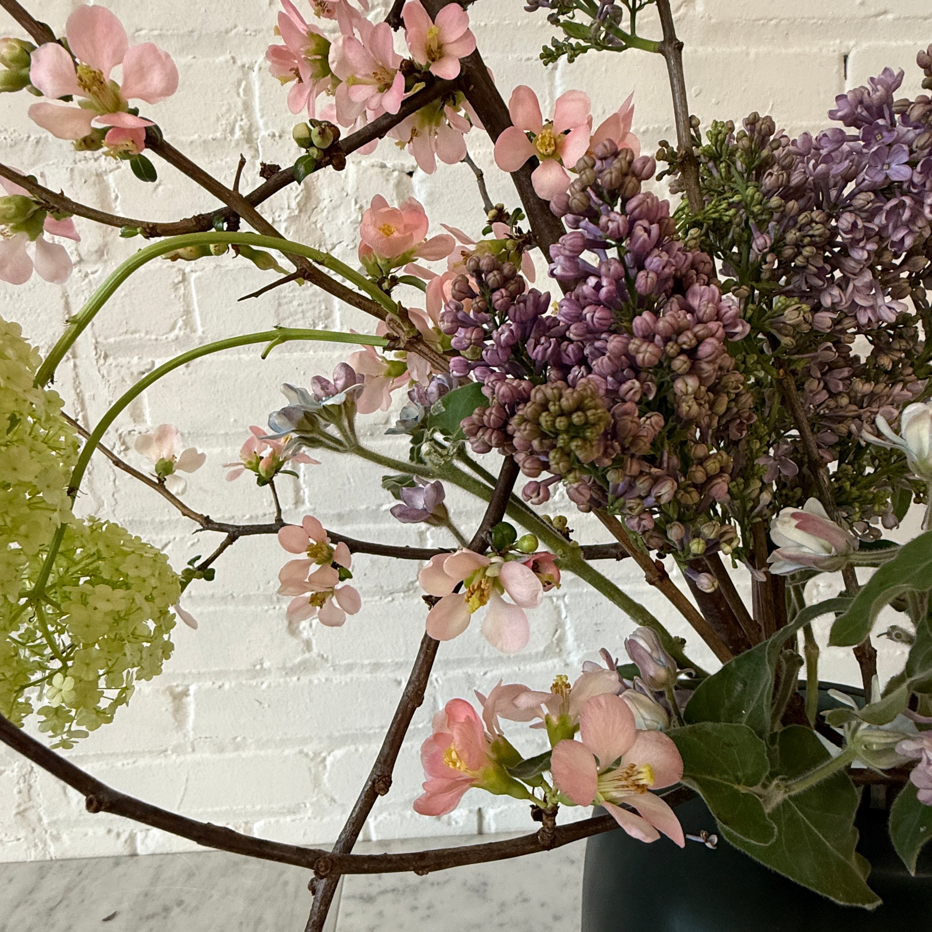 Floral arrangement with pink and purple flowers on a white brick wall background