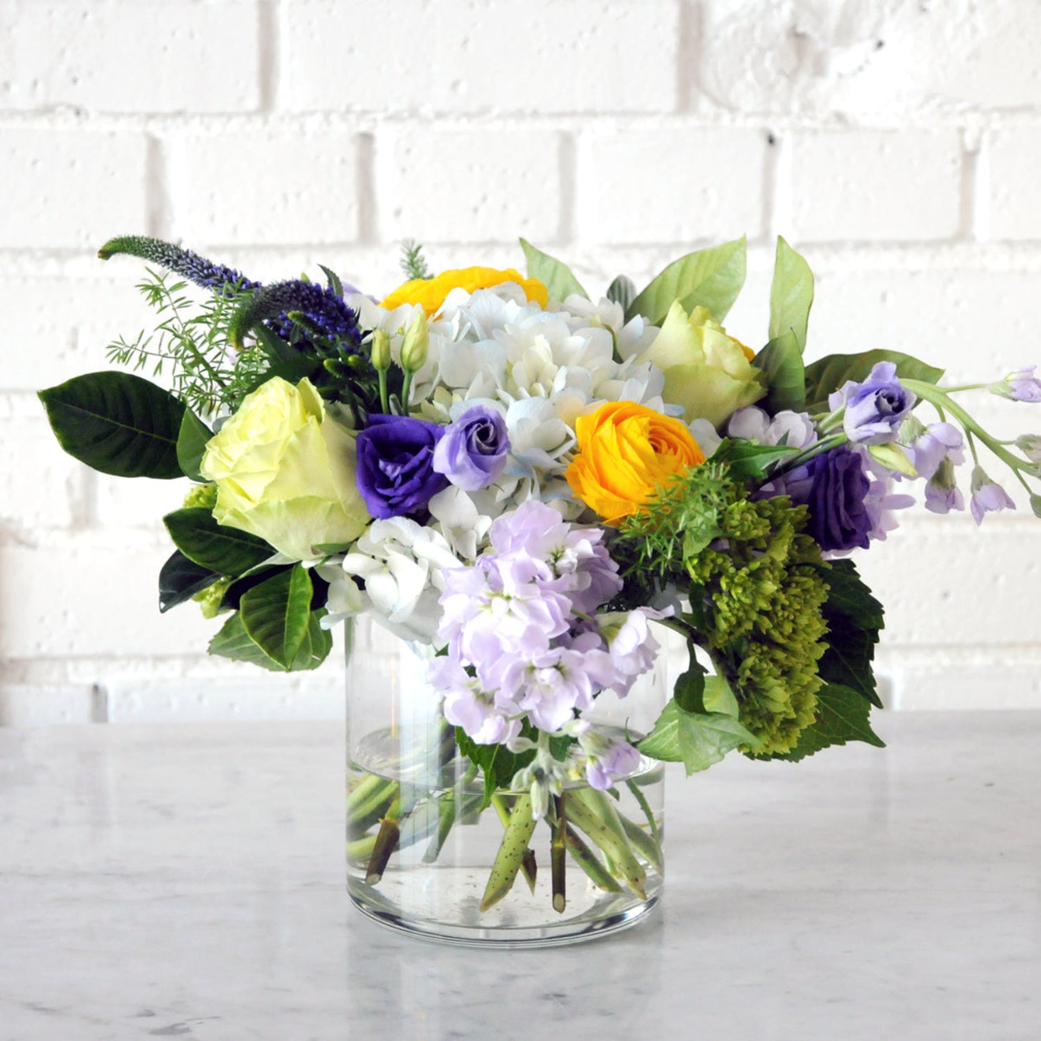 Bright yellow Ranunculus, Liliac Stock and Playa Blanca Rosses  styled Creative Director Classic  image is an example of the styling rather than the exact arrangement that will be sent 