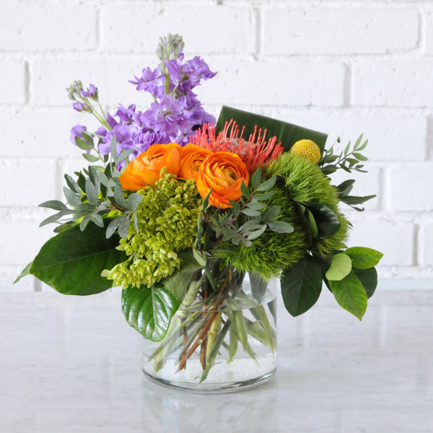 Front view of fresh floral arrangement featuring vibrant oranges and purples. Image is an example of the styling rather than the exact arrangement that will be sent 