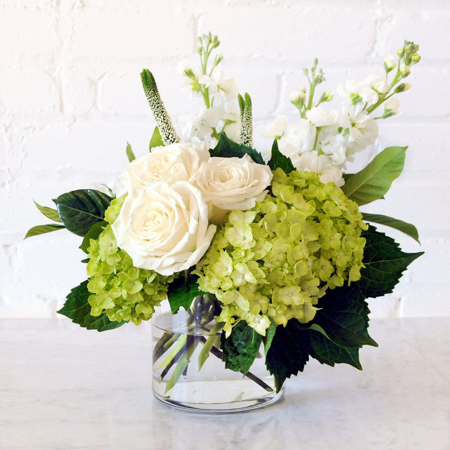 Spruce Flowers Duke arrangement showing Mini Green Hydrangea, White roses and Stock in a clear glass vase.