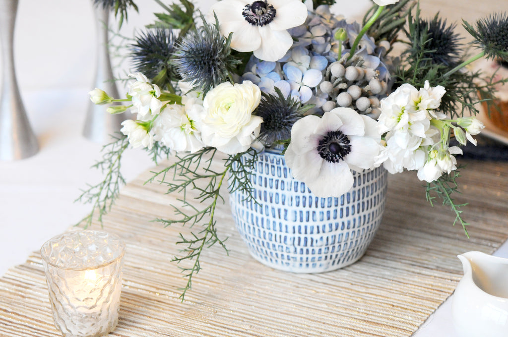 Freemont flower arrangement in subtle white blue tones shown as a table center with votives on a table runner