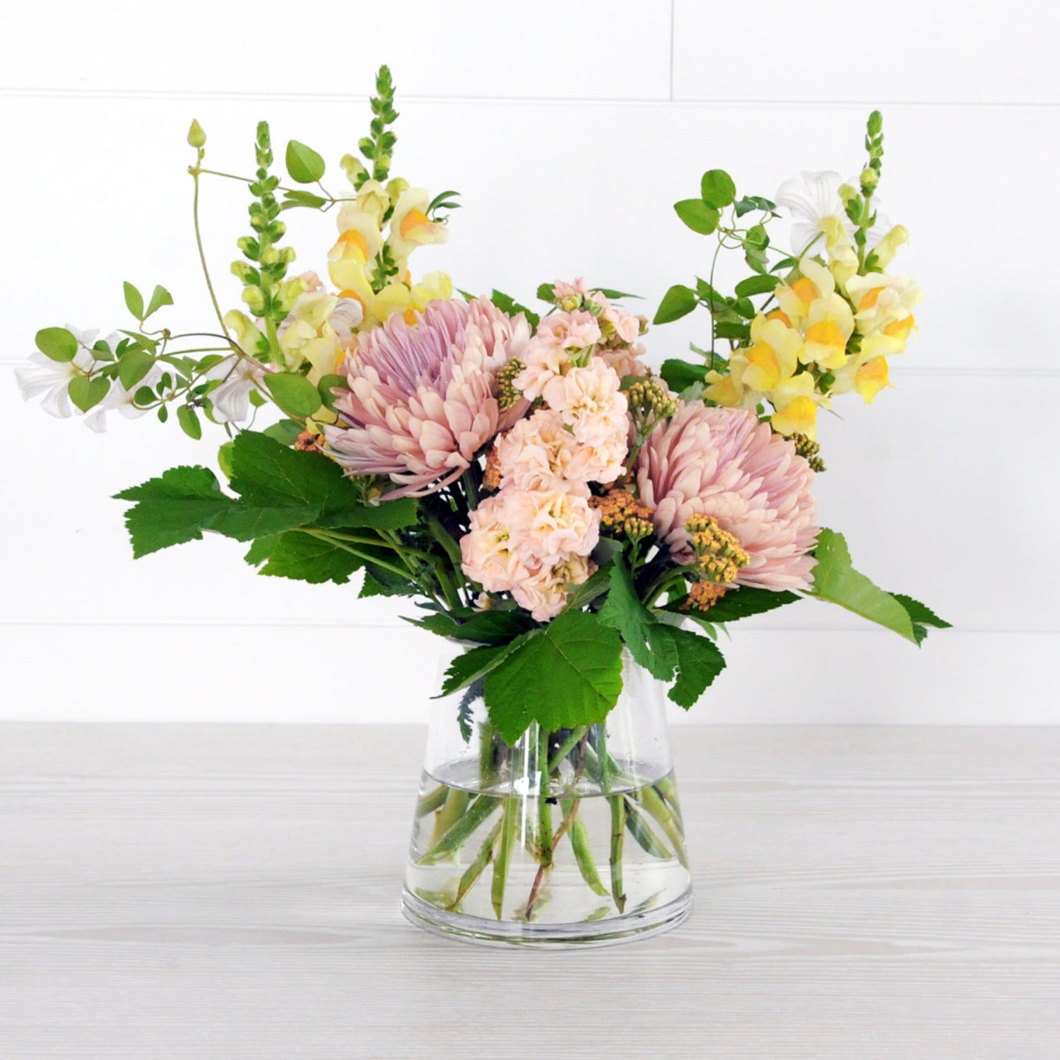 An example of the Larpenteur arrangement featuring stock, snapdragons, and yarrow in a pyramid clear glass vase